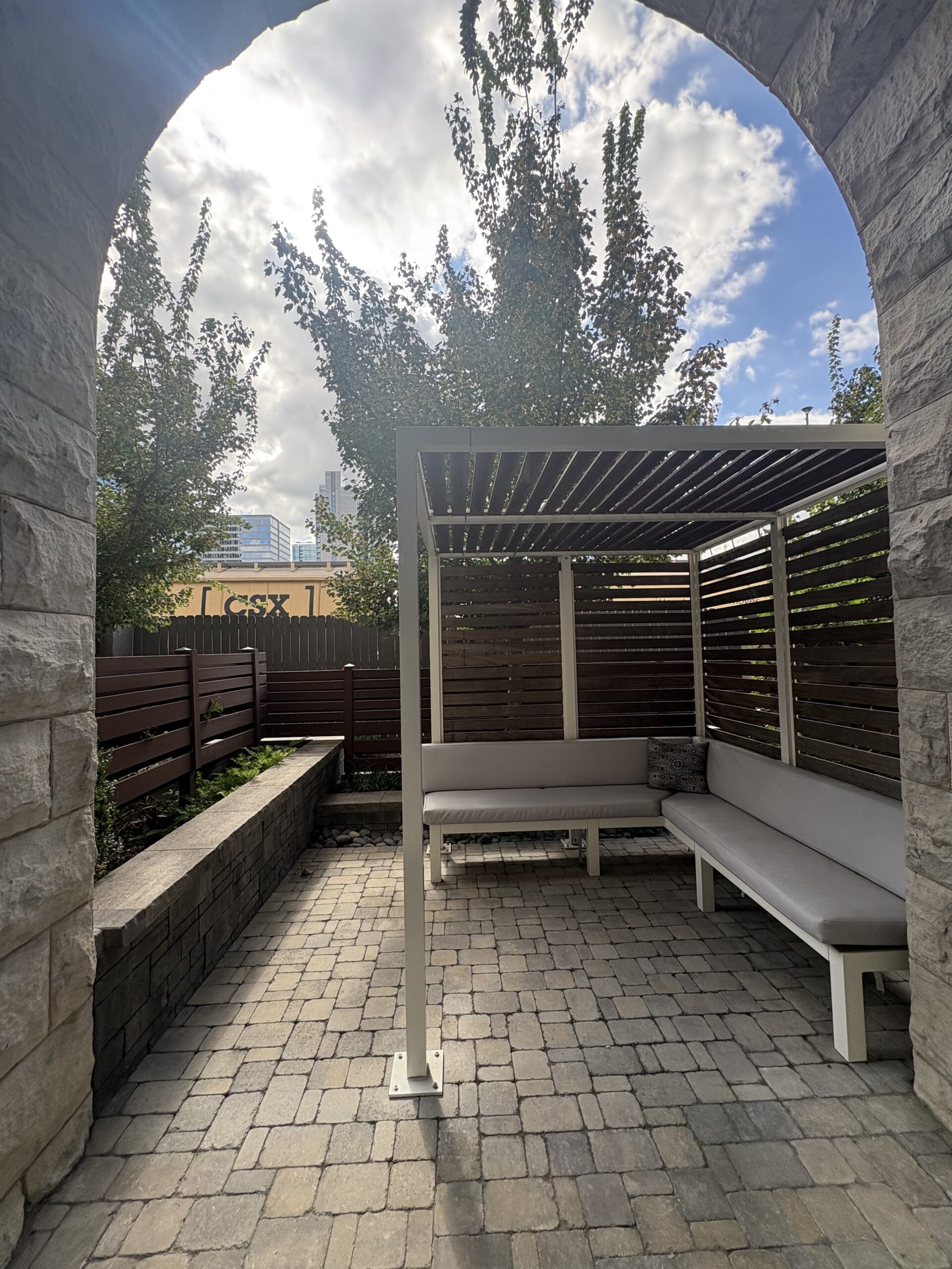 Private hotel patio with pergola and cushioned bench framed by a limestone archway, Nashville skyline beyond