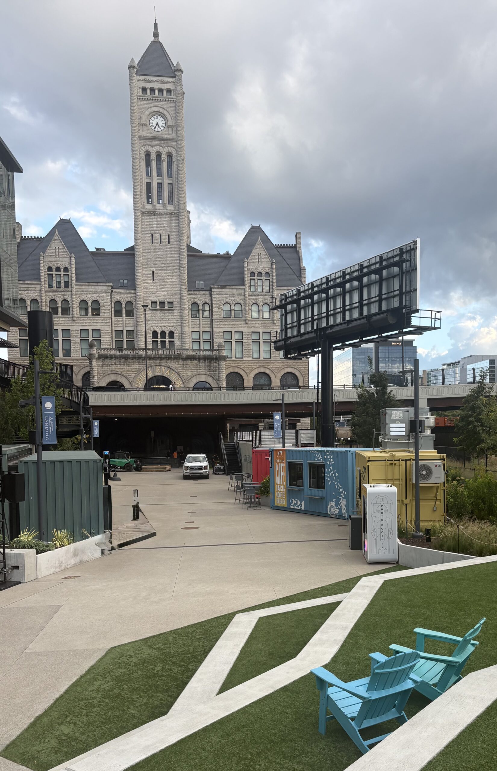 Union Station clock tower and stone facade with gold lettering, seen from the Nashville Yards lawn with teal Adirondack chairs