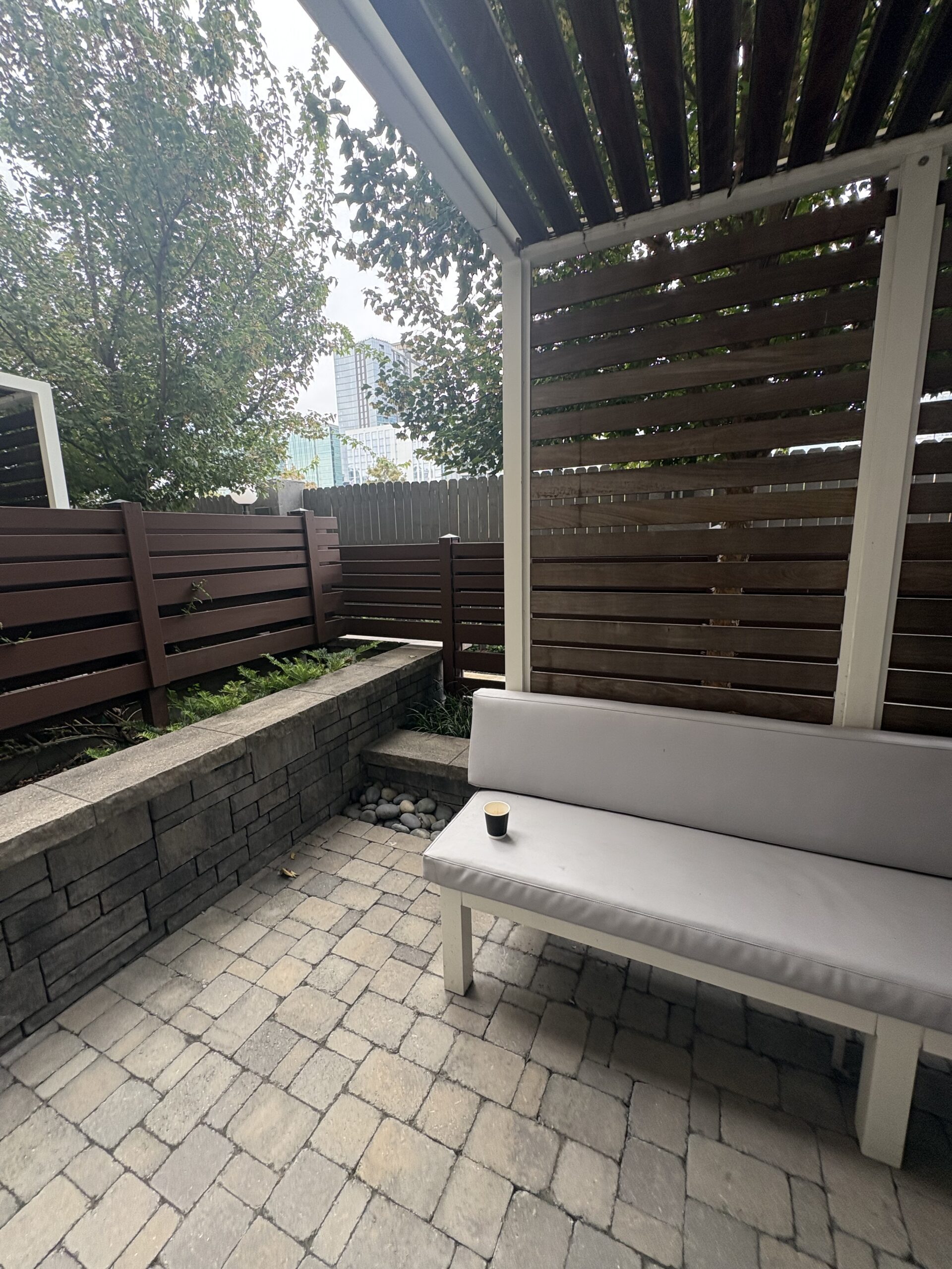 Private hotel patio with pergola, cushioned bench, espresso cup, and Nashville skyline beyond the trees