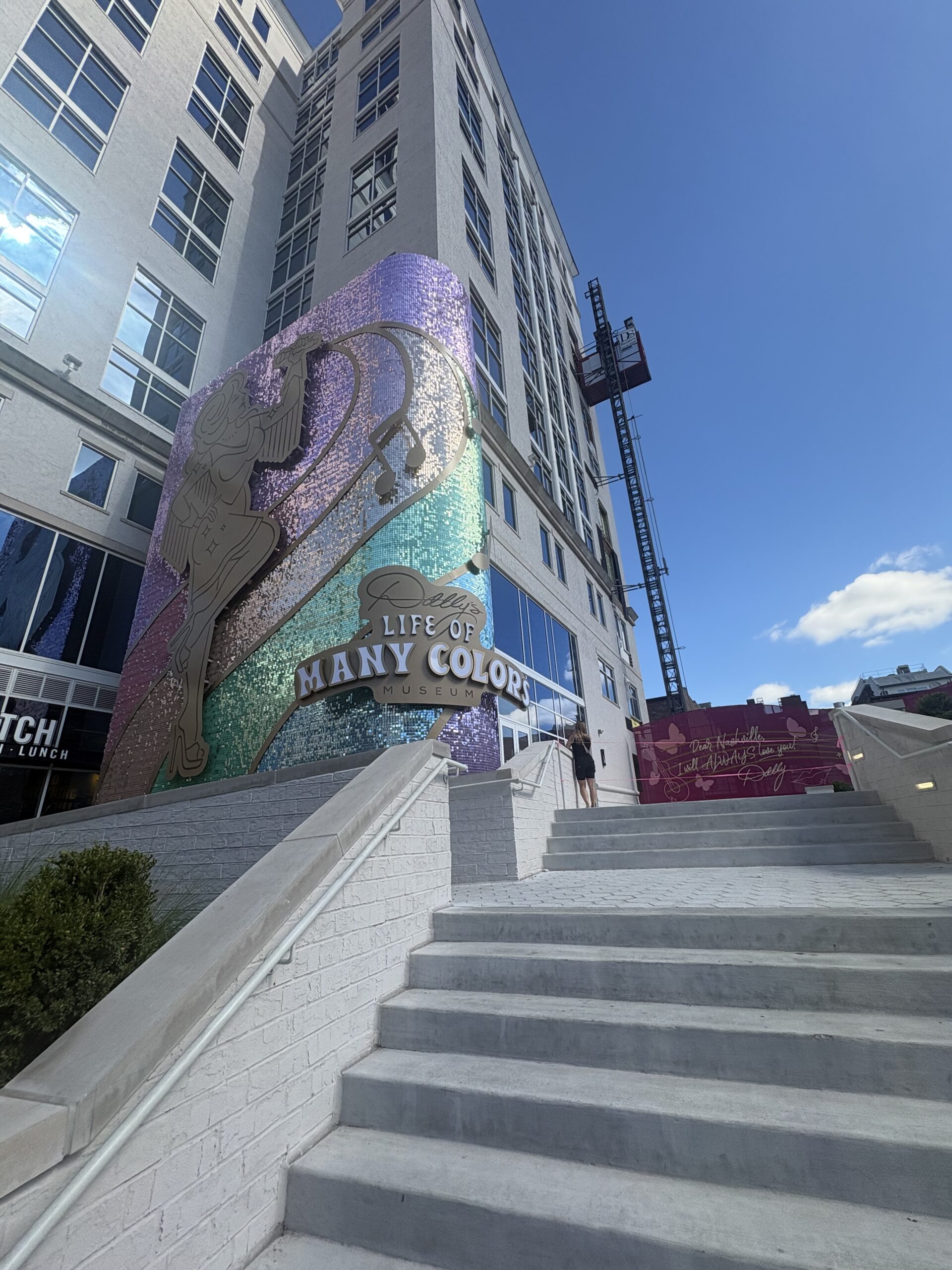 Sequined rainbow facade with a gold Dolly silhouette and the Life of Many Colors Museum sign at the museum entrance on 3rd Avenue North in Nashville