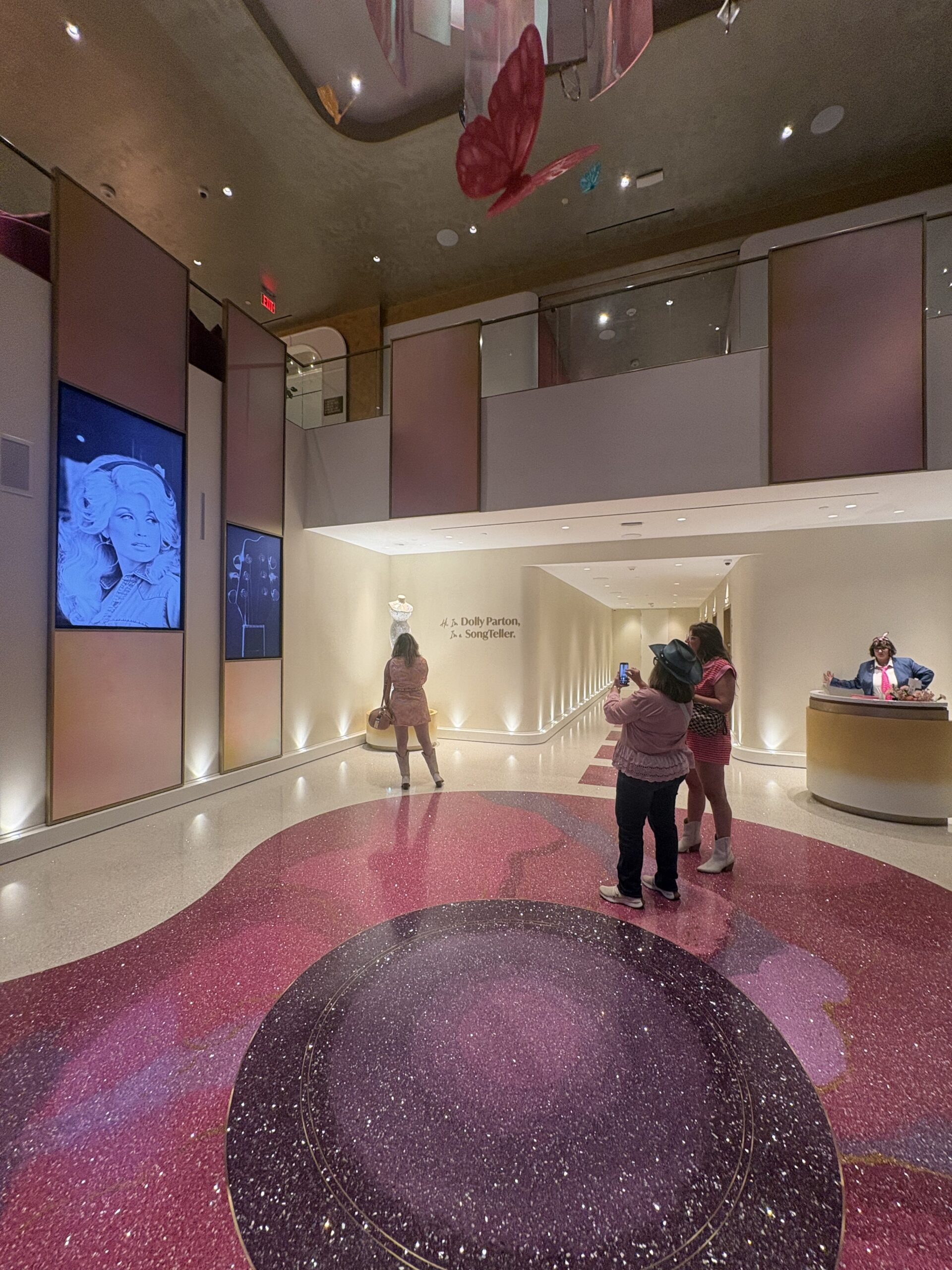 SongTeller Hotel lobby with a sparkling pink and purple floor, butterfly chandelier, and Dolly Parton gown display