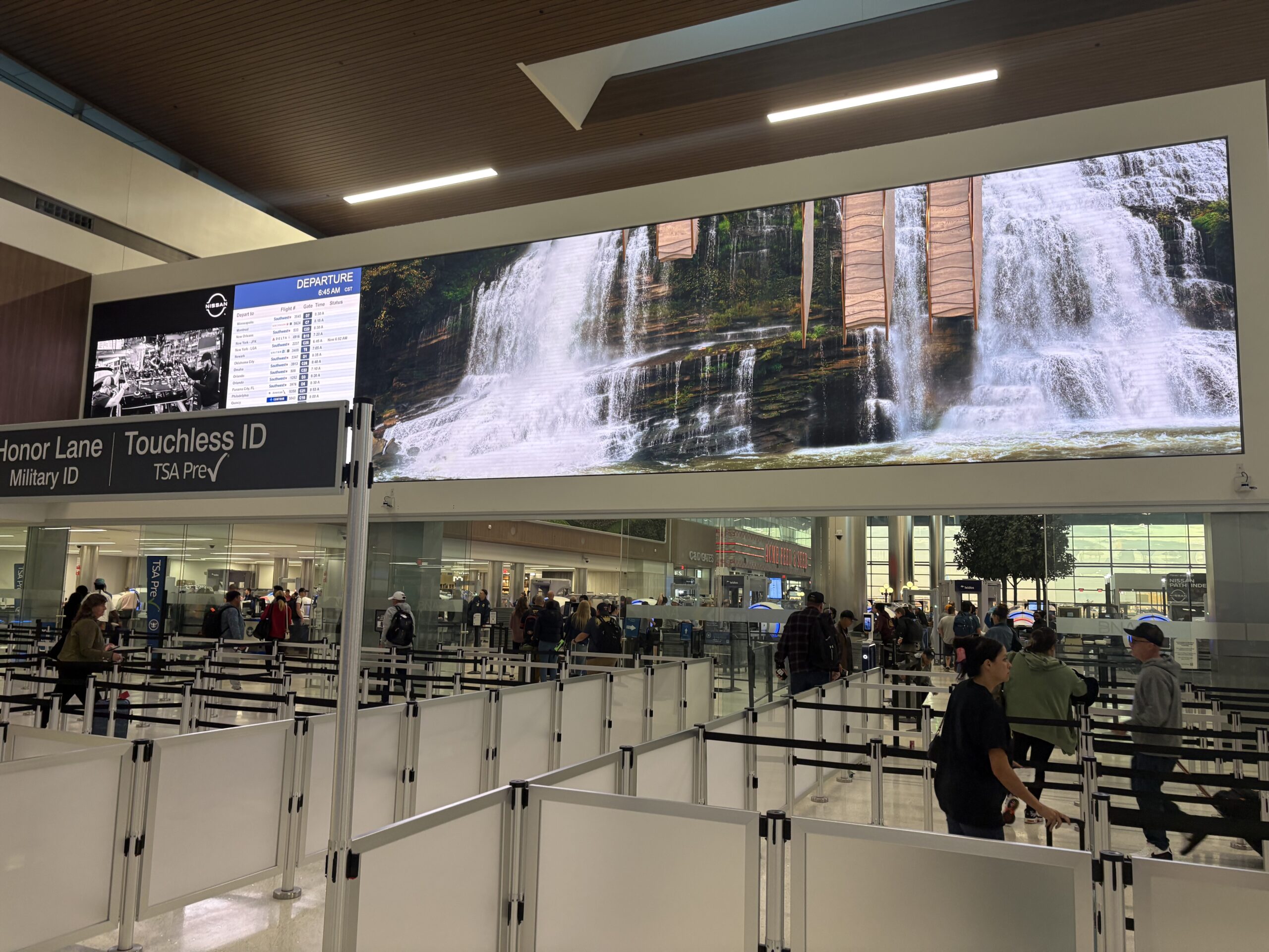 Security checkpoint at BNA under a wide waterfall video screen, with Honor Lane and Touchless ID TSA PreCheck signs