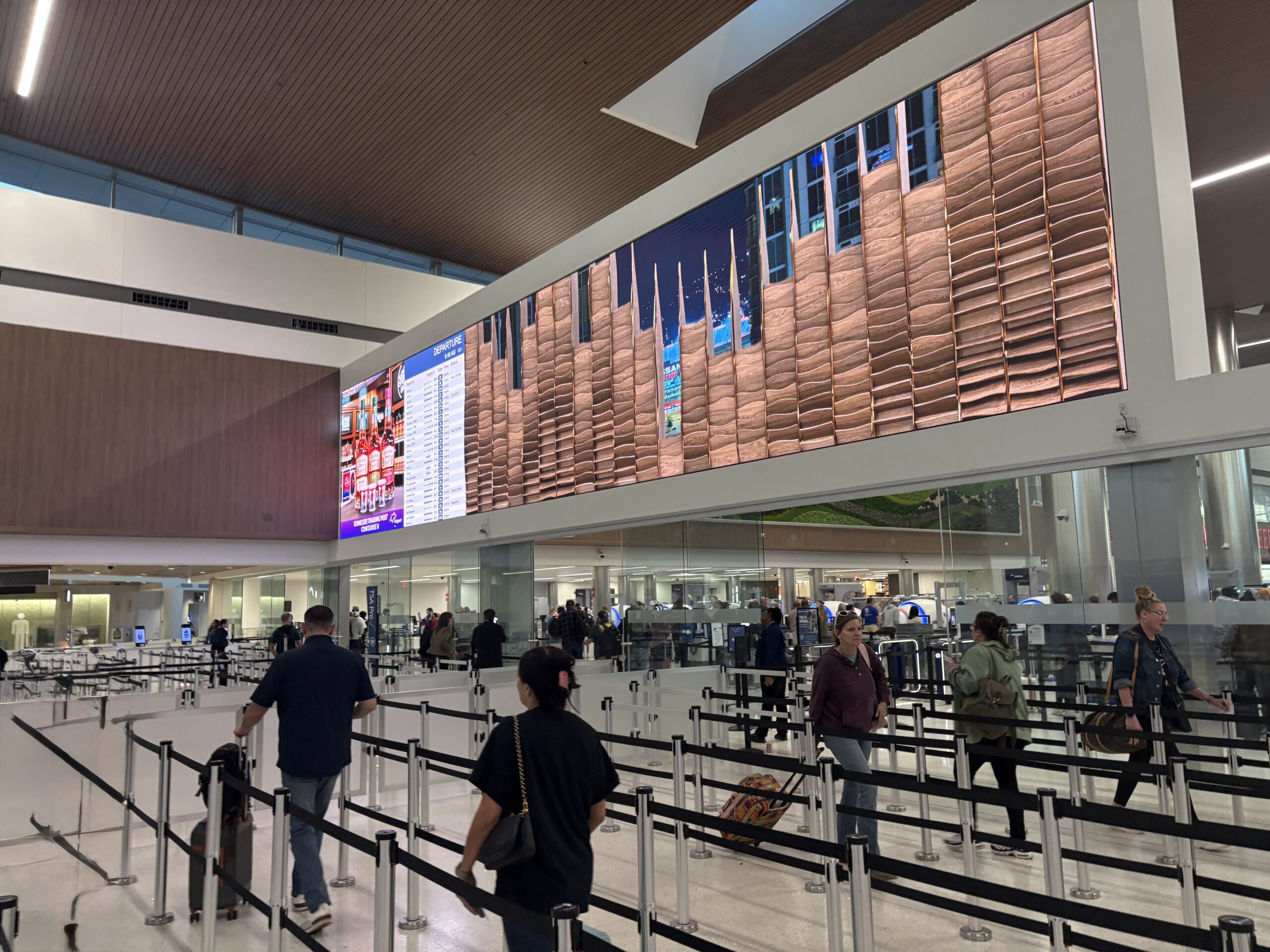 Departures hall at Nashville International Airport with a giant copper-toned digital wall above the security checkpoint