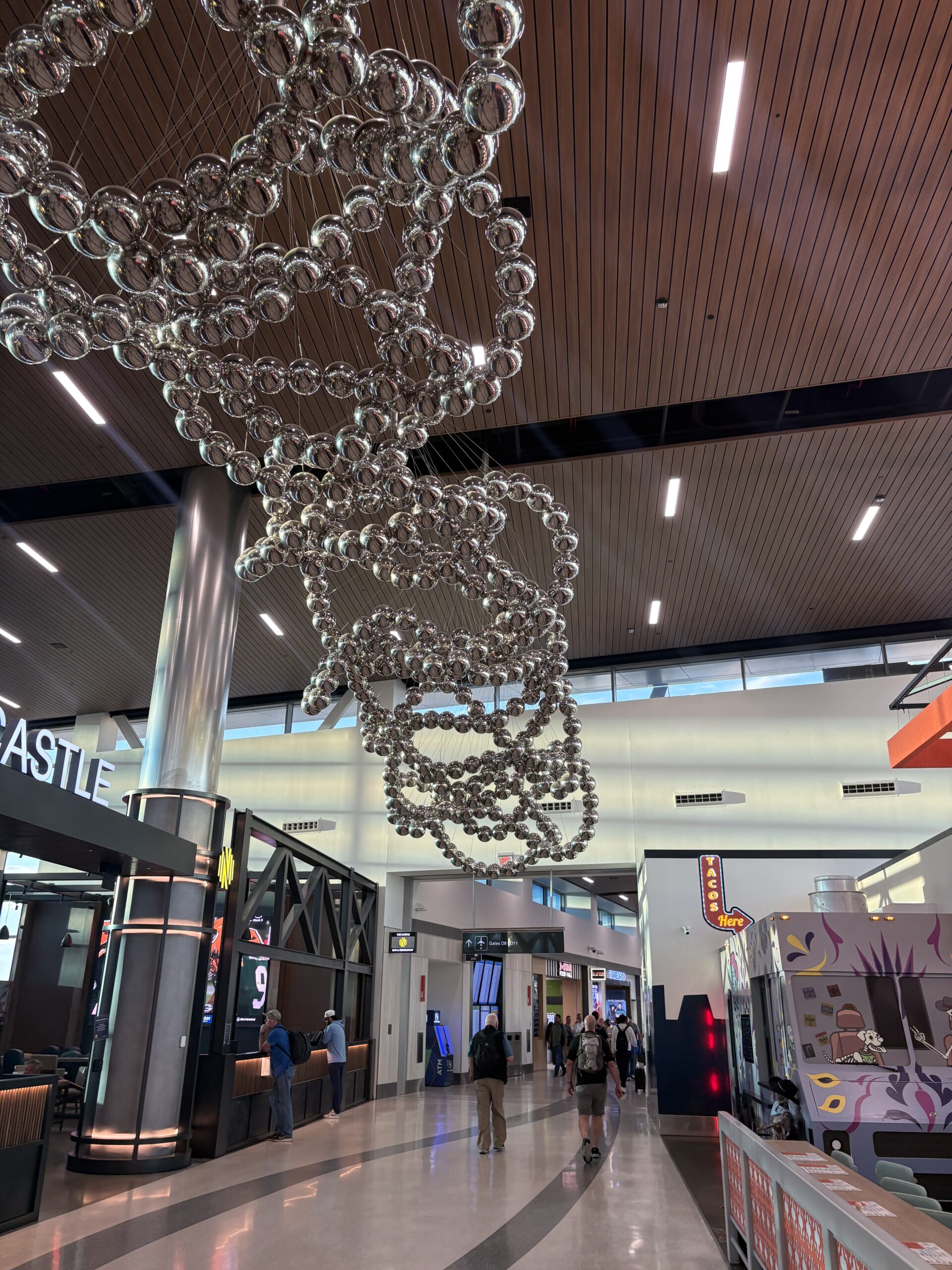 Concourse D at Nashville International Airport with a hanging silver sphere sculpture, The Castle restaurant and a taco counter styled like a food truck